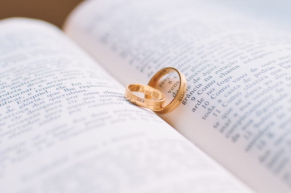 two gold wedding rings resting on an open book, symbolizing love and commitment amidst the printed text