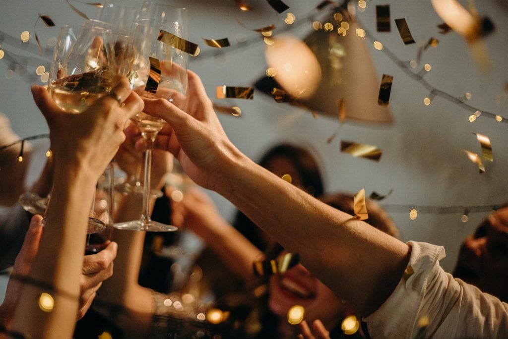 a lively celebration with hands raising champagne glasses amid golden confetti and warm lights, capturing a joyful moment of togetherness