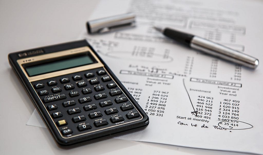 a calculator rests beside financial documents and a pen, featuring handwritten notes and calculations