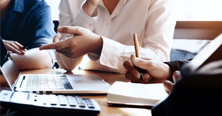 two people engaged in a discussion over a laptop, with one pointing and the other taking notes, highlighting a collaborative work session