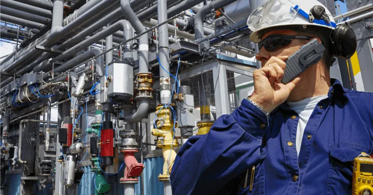 a worker in a blue uniform with safety equipment stands near complex industrial piping and machinery in a processing plant