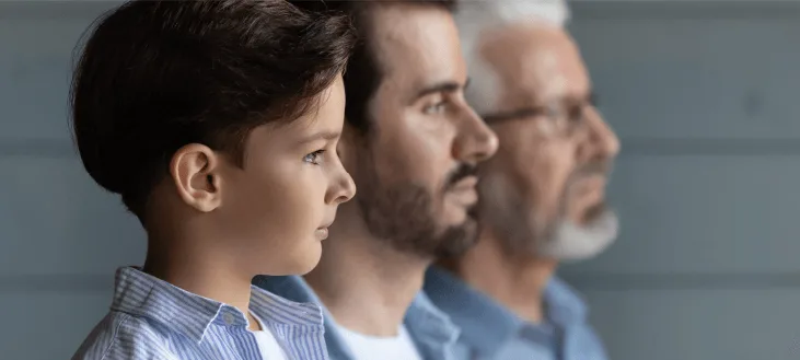 a young boy in a striped shirt stands next to two adults, all looking off-camera against a softly blurred background