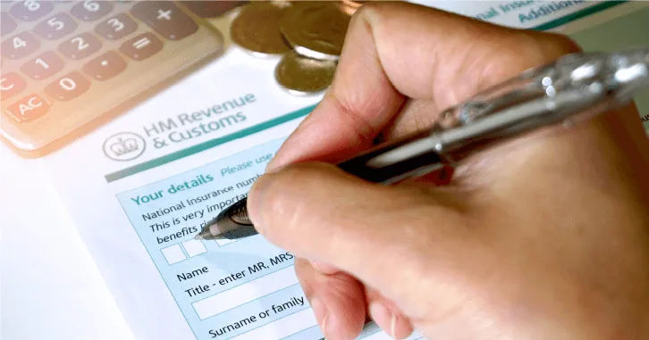 a hand holds a pen, filling out an HM Revenue & Customs form, with coins and a calculator nearby